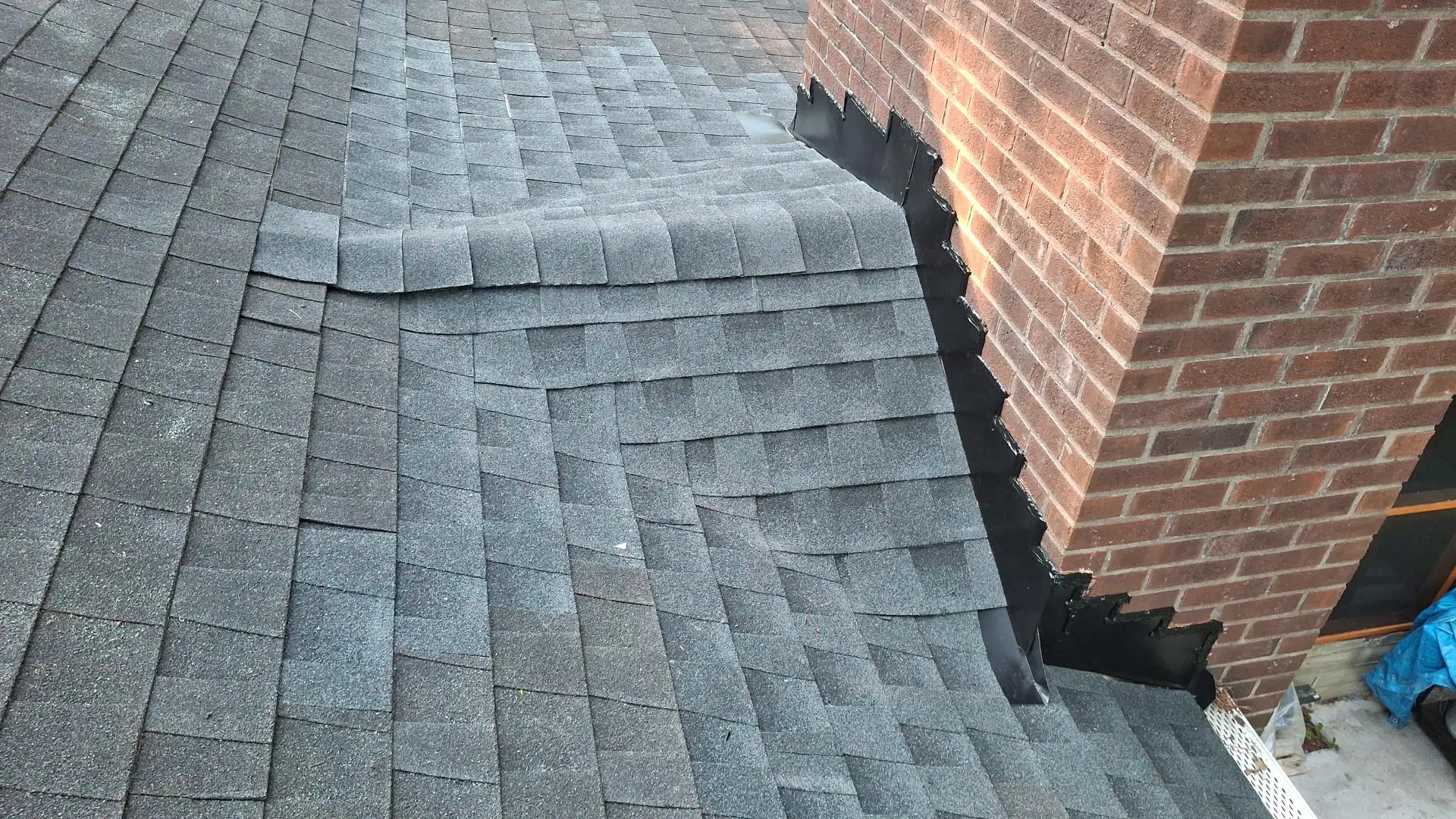 A gray shingled roof with a brick chimney on the right; step flashing along the chimney base.