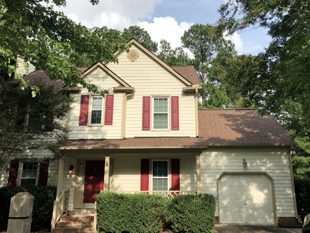 Home using accent colors for roof color - Small two-story house with cream siding, red shutters, and CertainTeed Landmark Burnt Sienna roof